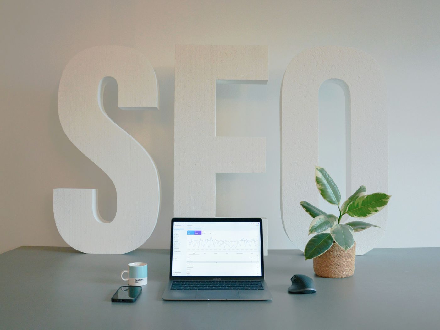 Large white SEO letters behind a desk with a laptop showing search performance data